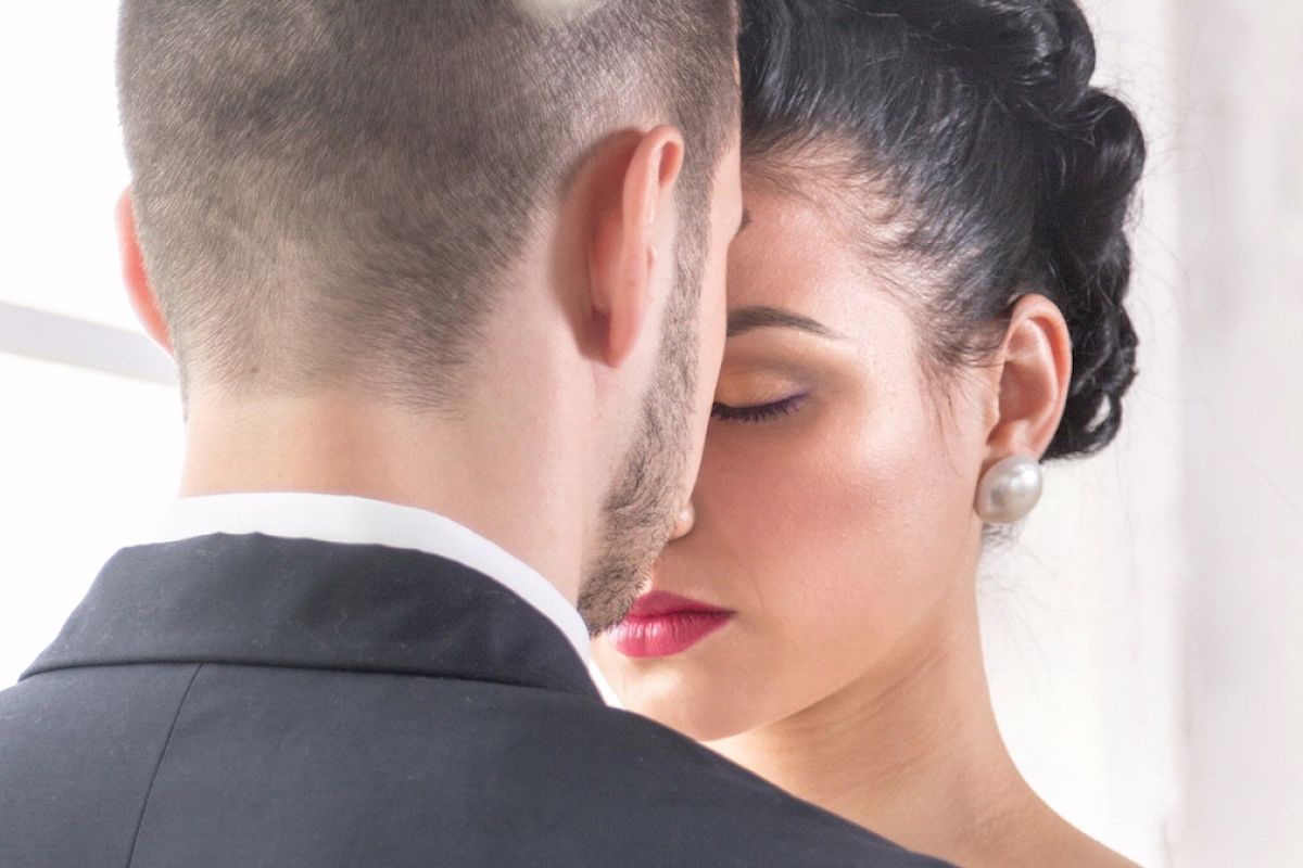 A close-up image shows a couple in an intimate moment, heads touching gently. The woman has closed eyes, wearing pearl earrings, and the man is in a suit.