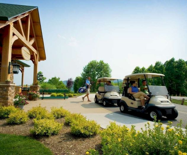 The image shows a golf course entrance with two golf carts, people, a building with green roof, and landscaped greenery.