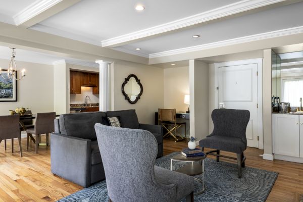 A modern living room with gray furniture, a wall mirror, a small workspace, and a view into a dining area and kitchen with wooden cabinetry.