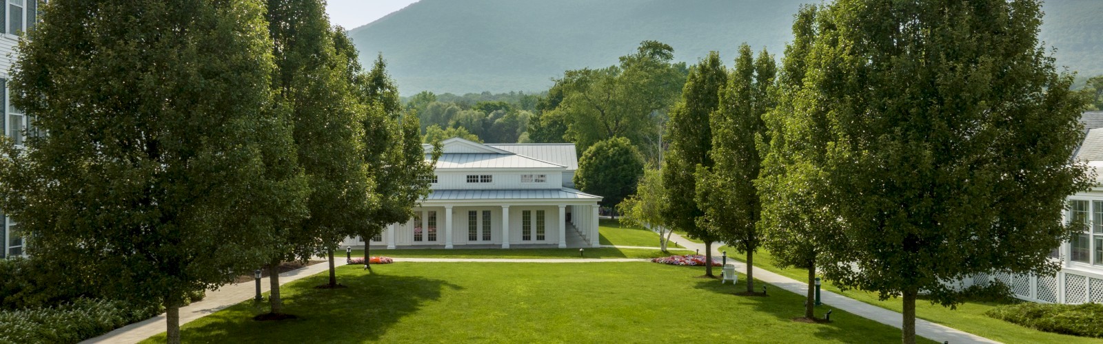 A golden retriever dog sits calmly outside a large white building with green shutters, under a blue sky with an American flag.