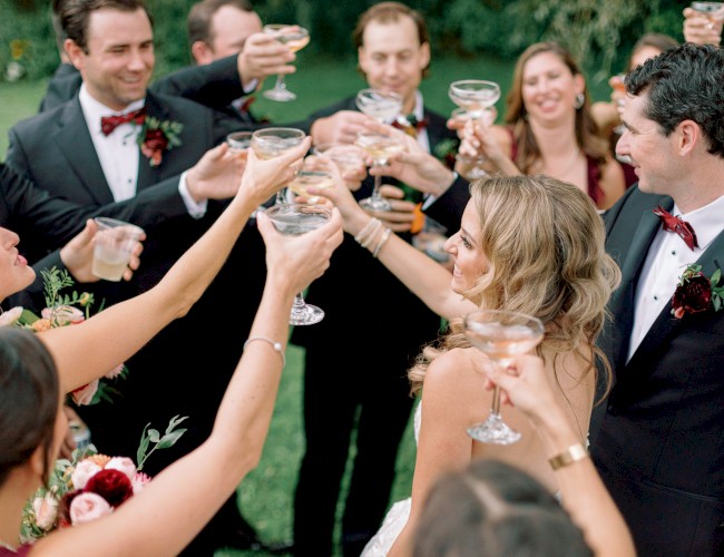 People toasting with drinks at a wedding celebration outdoors.
