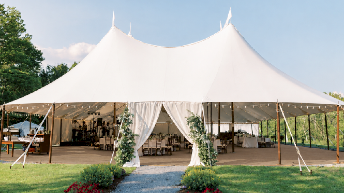 A large white event tent set up outdoors with tables, chairs, and decorations, possibly for a wedding or celebration.