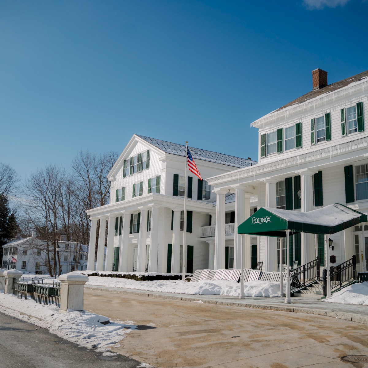 Large white colonial-style building with columns, US flag; snow on ground and trees, 