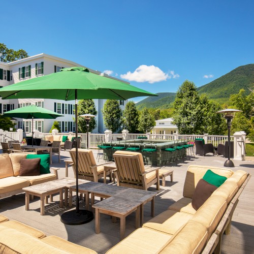 An outdoor patio with seating, umbrellas, trees, and mountains in the background on a sunny day.