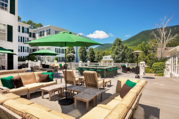 This is an outdoor terrace with lounge chairs, umbrellas, and a scenic mountain view on a sunny day.