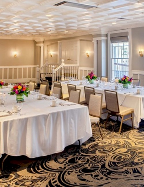 A beautifully set banquet or wedding reception with long tables, elegant floral arrangements, and soft natural light in a stylish room.