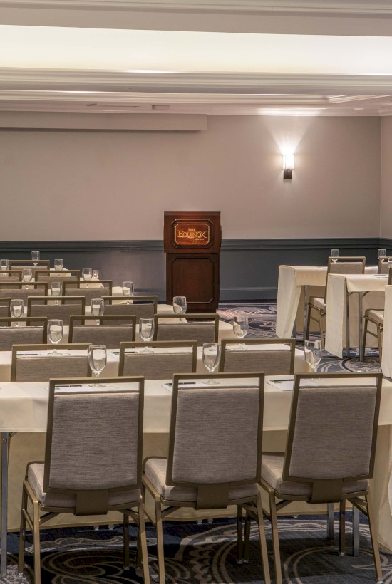 A conference room or banquet hall set up with tables, chairs, glassware, and pitchers, ready for a formal event or meeting.