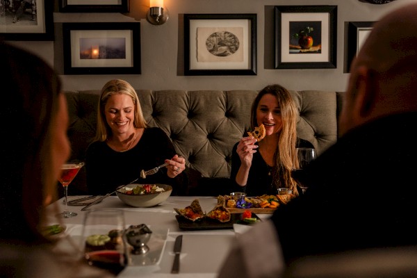 A group of people enjoying a meal together in a cozy restaurant setting, with framed art on the wall and food on the table.