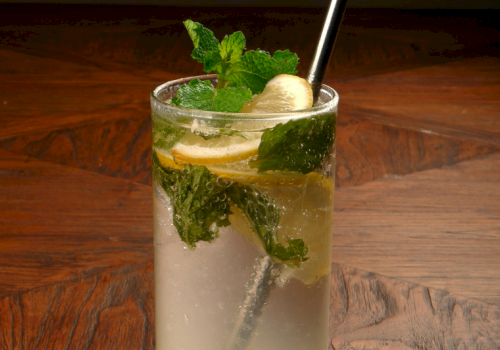 A refreshing glass of lemonade with mint leaves and banana slices on a wooden table.