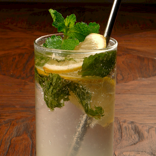 A refreshing glass of lemonade with mint leaves and banana slices on a wooden table.