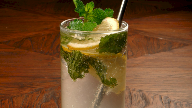 A refreshing glass of lemonade with mint leaves and banana slices on a wooden table.