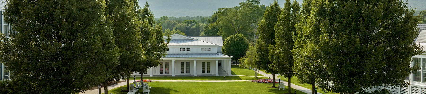 A peaceful garden with trees, colorful flowers, white benches, and scenic mountains in the background.