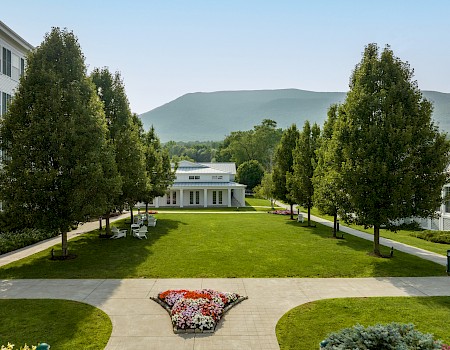 A peaceful garden with trees, colorful flowers, white benches, and scenic mountains in the background.