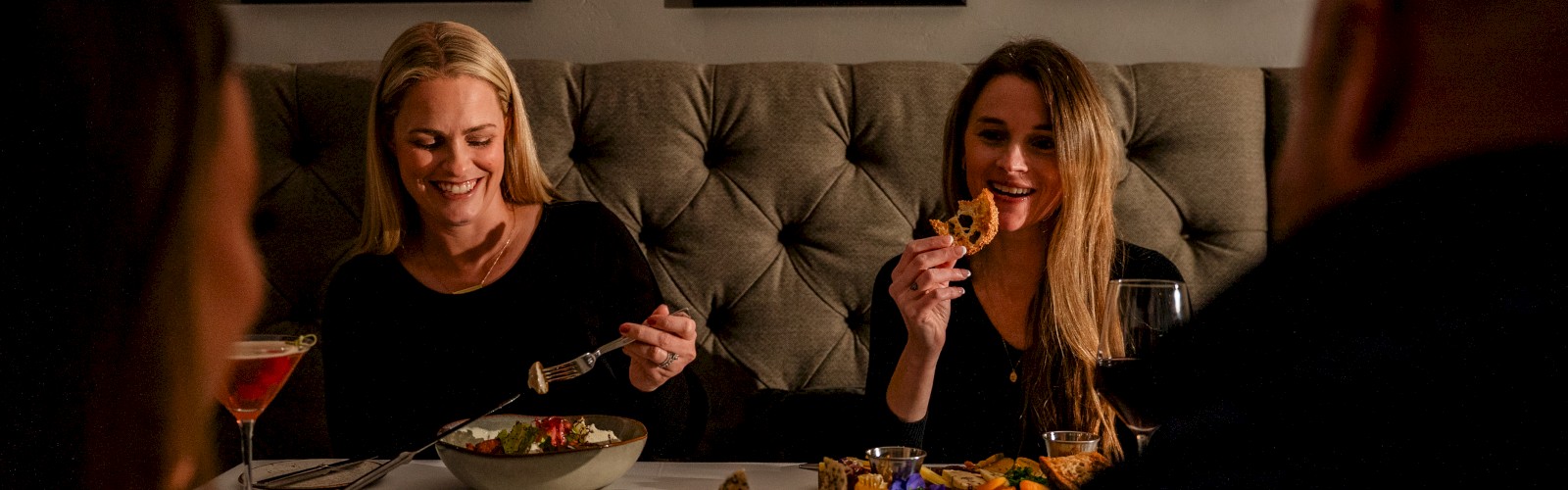 Four people enjoy a dinner together, smiling and eating delicious food in a cozy, art-decorated restaurant setting.