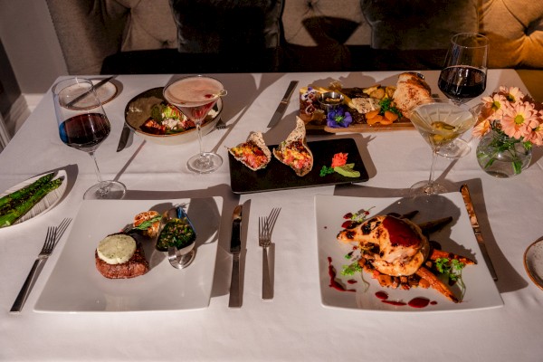 A fancy dinner table with various gourmet dishes, wine glasses, and a centerpiece of flowers, set for an elegant meal.