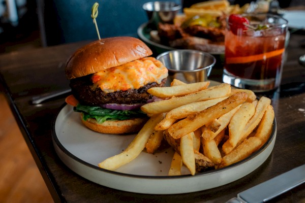 A burger with fries on a plate, served with ketchup and a drink with ice.