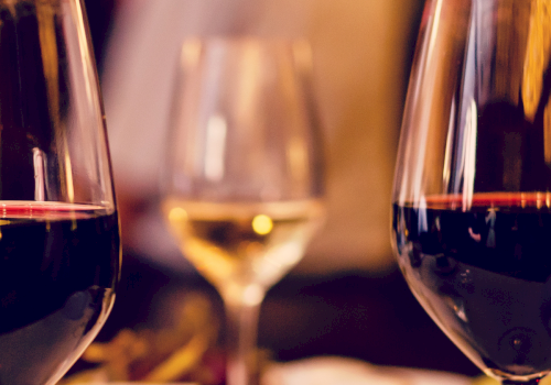 Three glasses filled with red and white wine are displayed, with a blurred background suggesting a cozy, elegant setting.