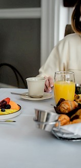A young girl and woman share a joyful breakfast together at a table filled with fruit, pastries, and drinks in a cozy dining setting.