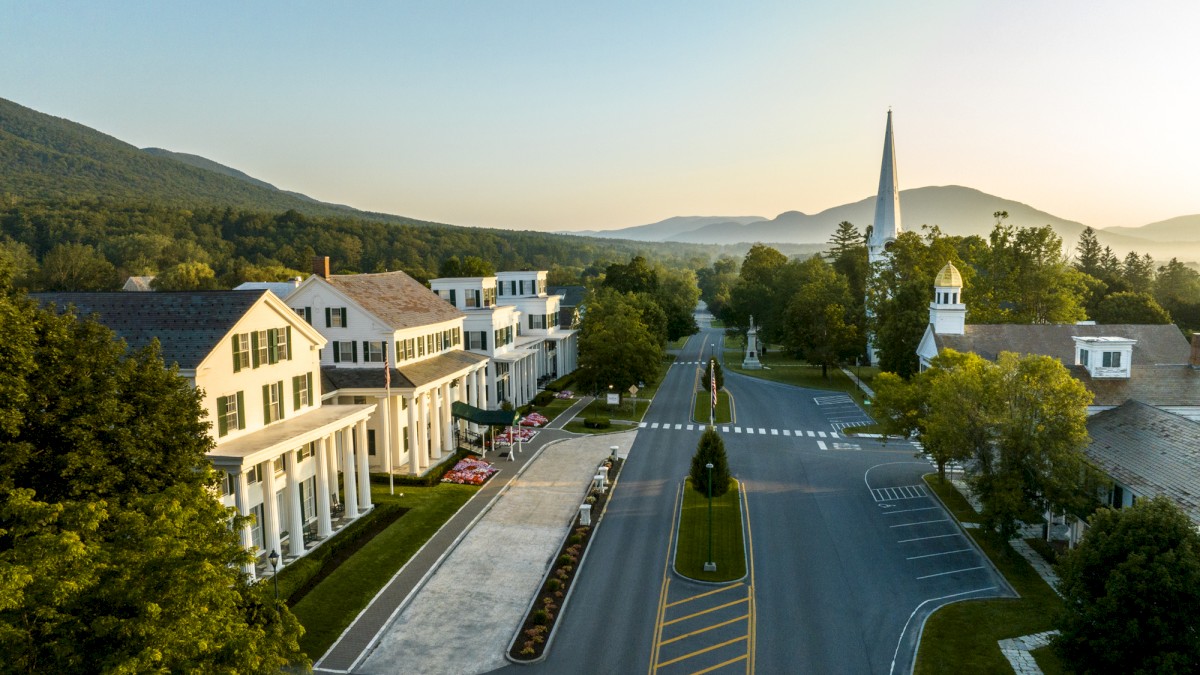 A quiet town with colonial-style buildings, church, mountains backdrop, and empty streets at sunrise or sunset.