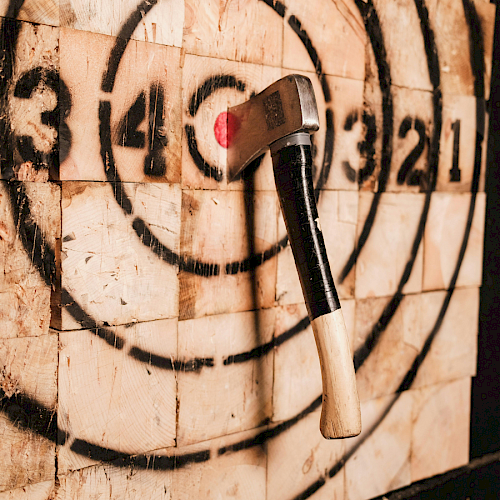 An axe embedded in a painted wood target, likely for axe throwing, with concentric circles numbered for scoring.