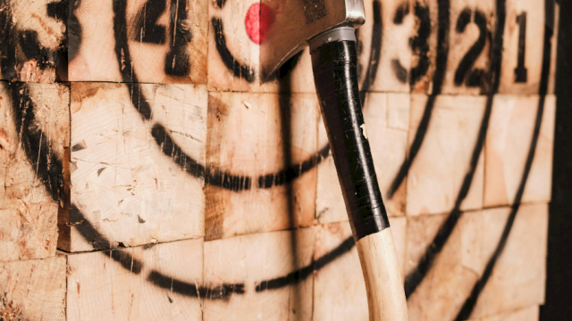 An axe embedded in a painted wood target, likely for axe throwing, with concentric circles numbered for scoring.