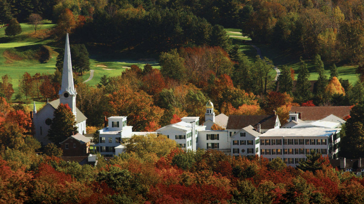 This image shows a small town or village surrounded by colorful autumn trees and a golf course in the background.
