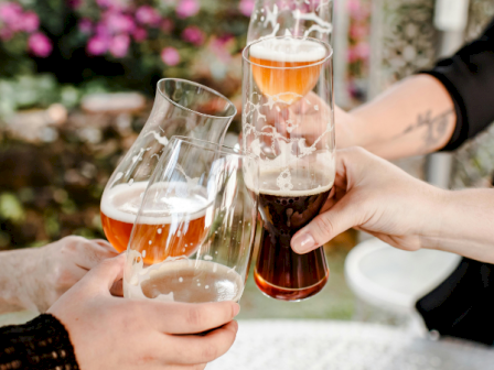 People are sharing a toast with glasses of rosé and beer outdoors, celebrating in a garden setting with flowers in the background.