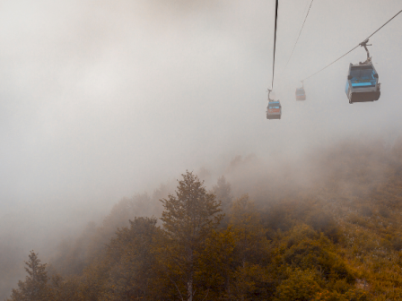 Cable cars ascend through fog above a forested landscape, creating a mysterious and scenic mountain view.