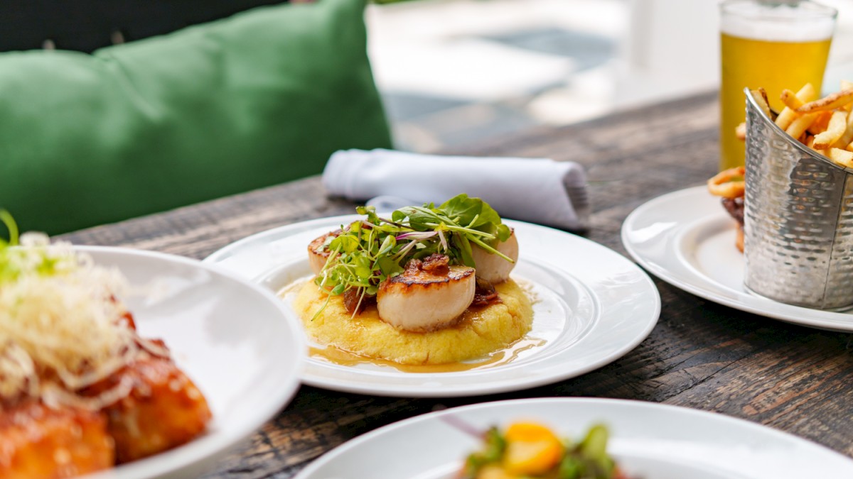 A beautifully presented outdoor meal featuring scallops, fries, drinks, and other gourmet dishes on a rustic wooden table.