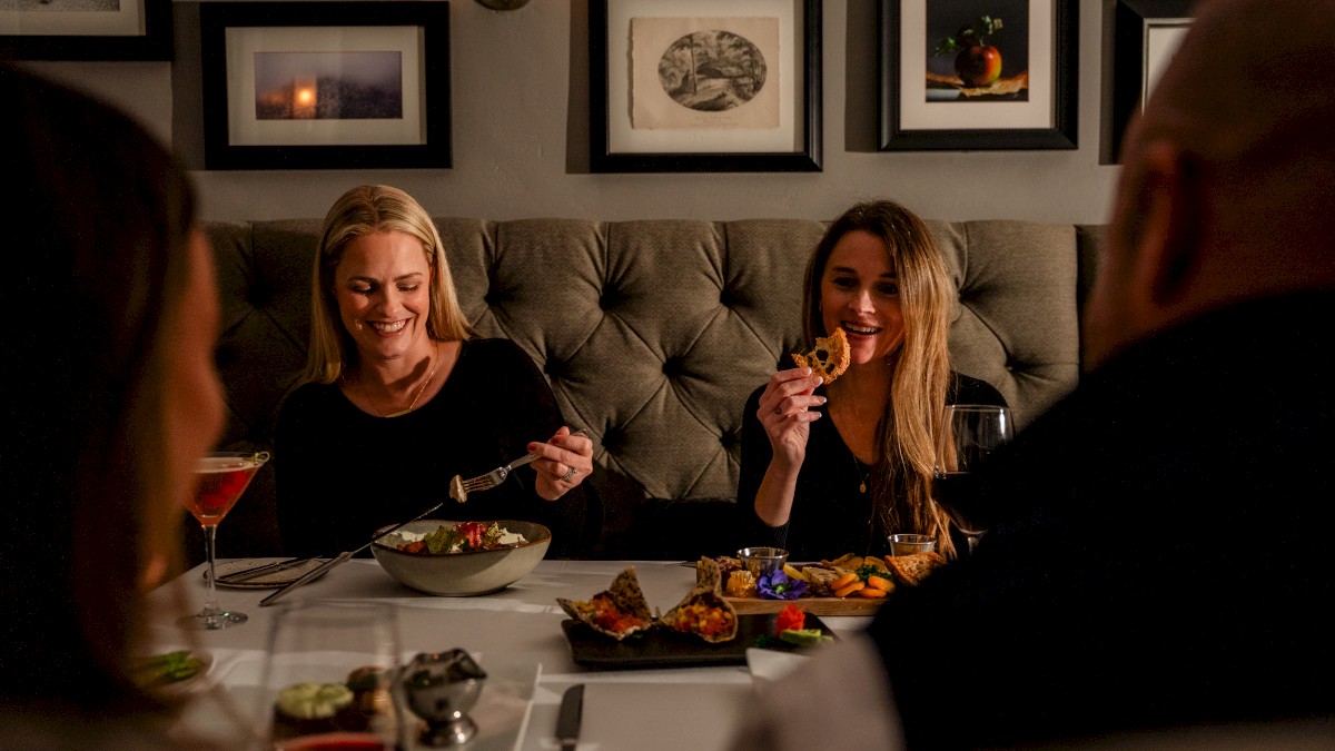 A group of five people enjoying a dinner together at a cozy, decorated restaurant, smiling and sharing food around the table.