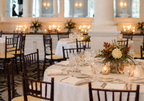 This image shows an elegant banquet hall decorated for a special event with round tables, floral centerpieces, and warm lighting.