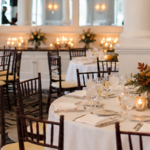 This image shows an elegant banquet hall decorated for a special event with round tables, floral centerpieces, and warm lighting.