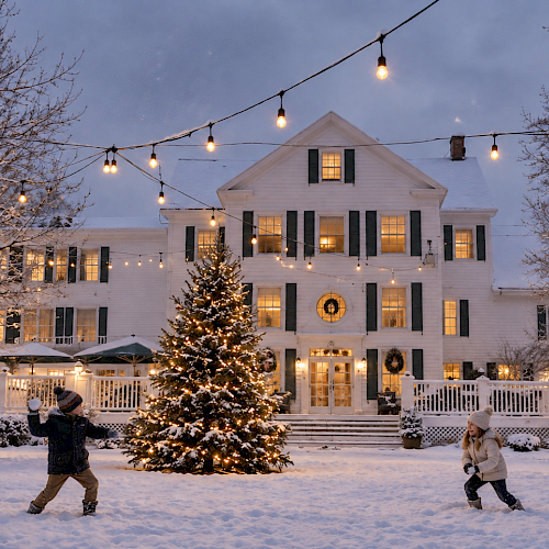Children playing in the snow in front of a decorated house with Christmas lights, a Christmas tree, and snow-covered trees at dusk.