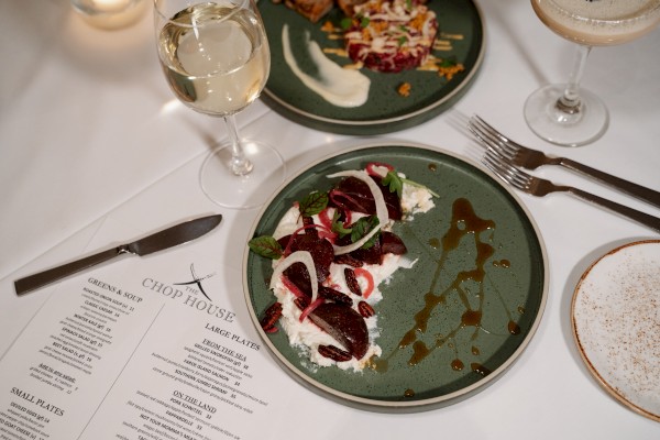 A dinner table with plates of food, wine glasses, a menu, and utensils at a restaurant setting.