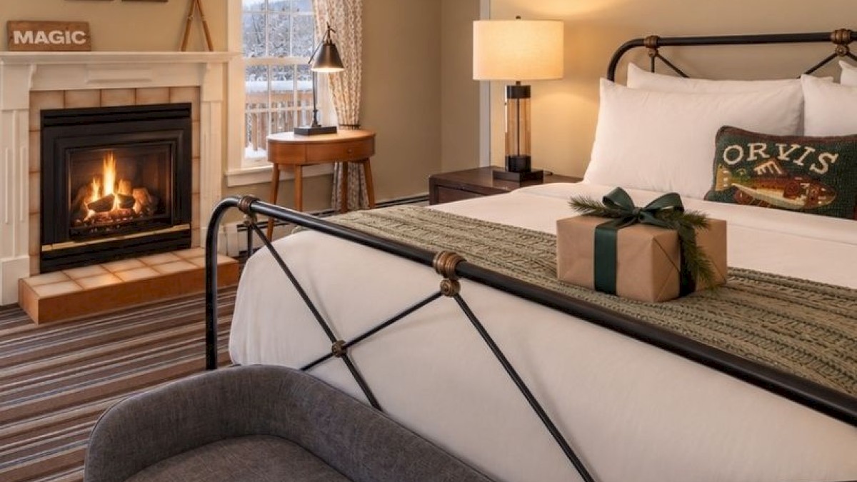 A cozy bedroom with a fireplace, a bed with a gift box, and warm lighting, creating a festive and inviting atmosphere inside.