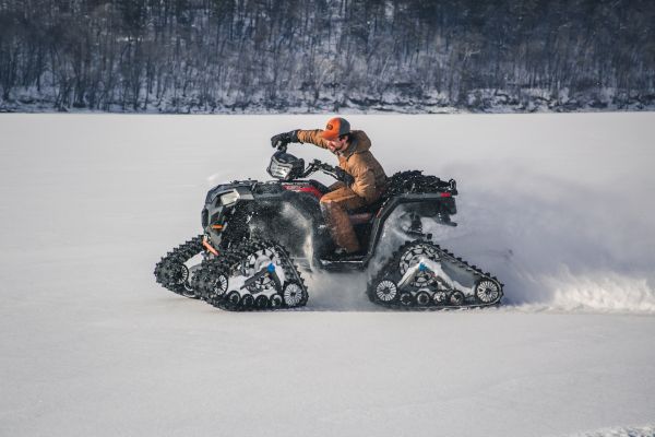 A person in winter attire is riding a snowmobile with caterpillar tracks across a snow-covered landscape.