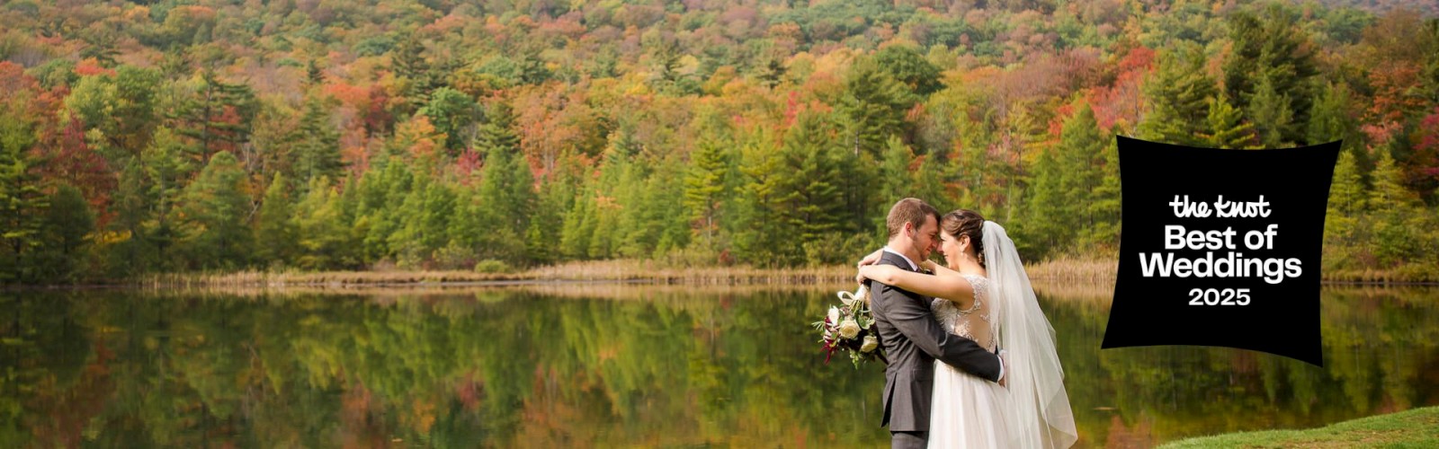 A couple embraces by a lake with a forest and mountains in the background. A badge says 