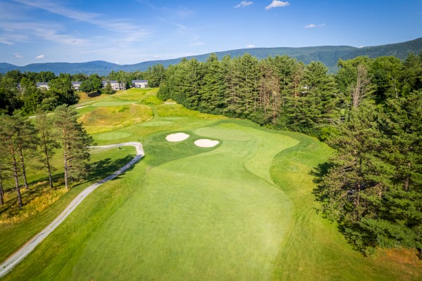 Aerial view of a golf course with green fairways, sand bunkers, and surrounding trees on a clear day.
