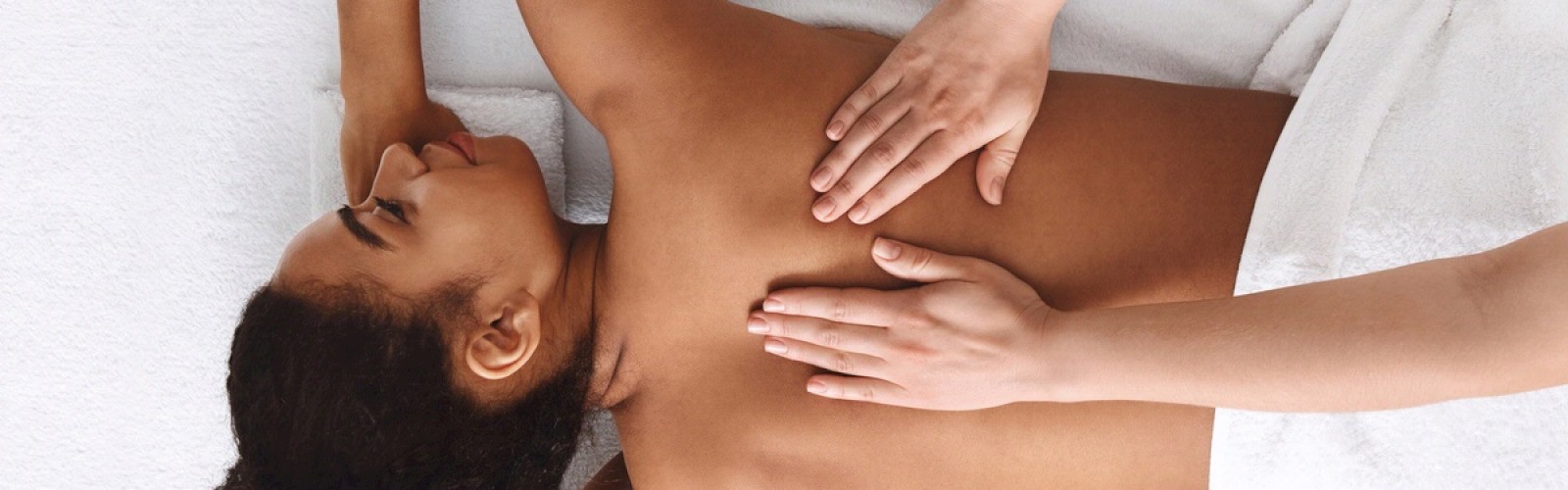 The image shows a person lying face down on a massage table while receiving a back massage from another person. The scene appears calm and relaxing.