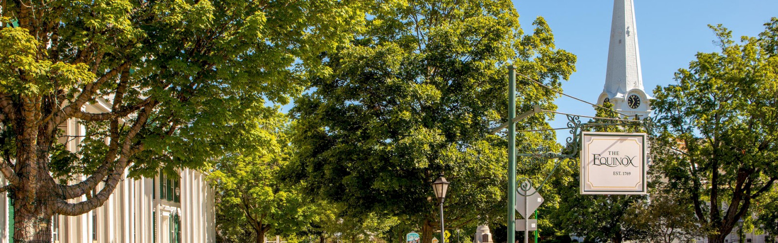 A serene street with lush trees, a sidewalk, a church with a steeple, and a sign reading 