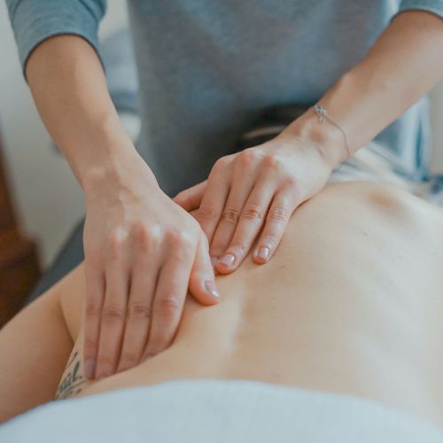 A person is receiving a back massage from someone wearing a grey long-sleeved shirt, using both hands to apply pressure on the back.
