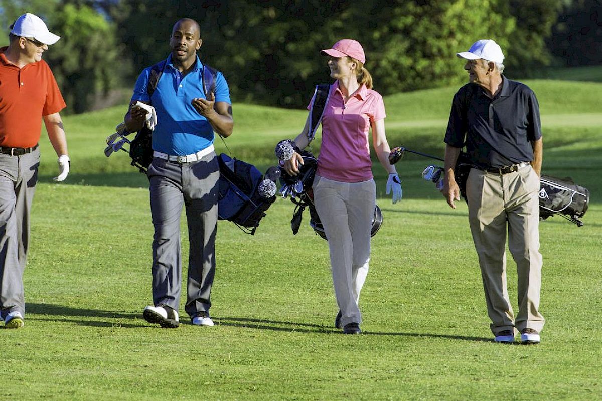 Four people are walking on a golf course, carrying golf bags and wearing golf attire, while engaging in conversation and enjoying the outdoor setting.