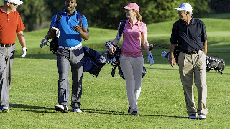 Four people are walking on a golf course, carrying golf bags and wearing golf attire, while engaging in conversation and enjoying the outdoor setting.