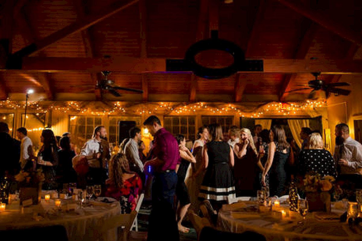 People are gathered at an indoor event with decorations and dim lighting, likely a party or wedding reception, enjoying socializing and dancing.