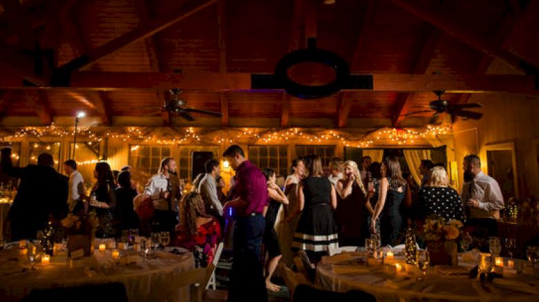 People are gathered at an indoor event with decorations and dim lighting, likely a party or wedding reception, enjoying socializing and dancing.