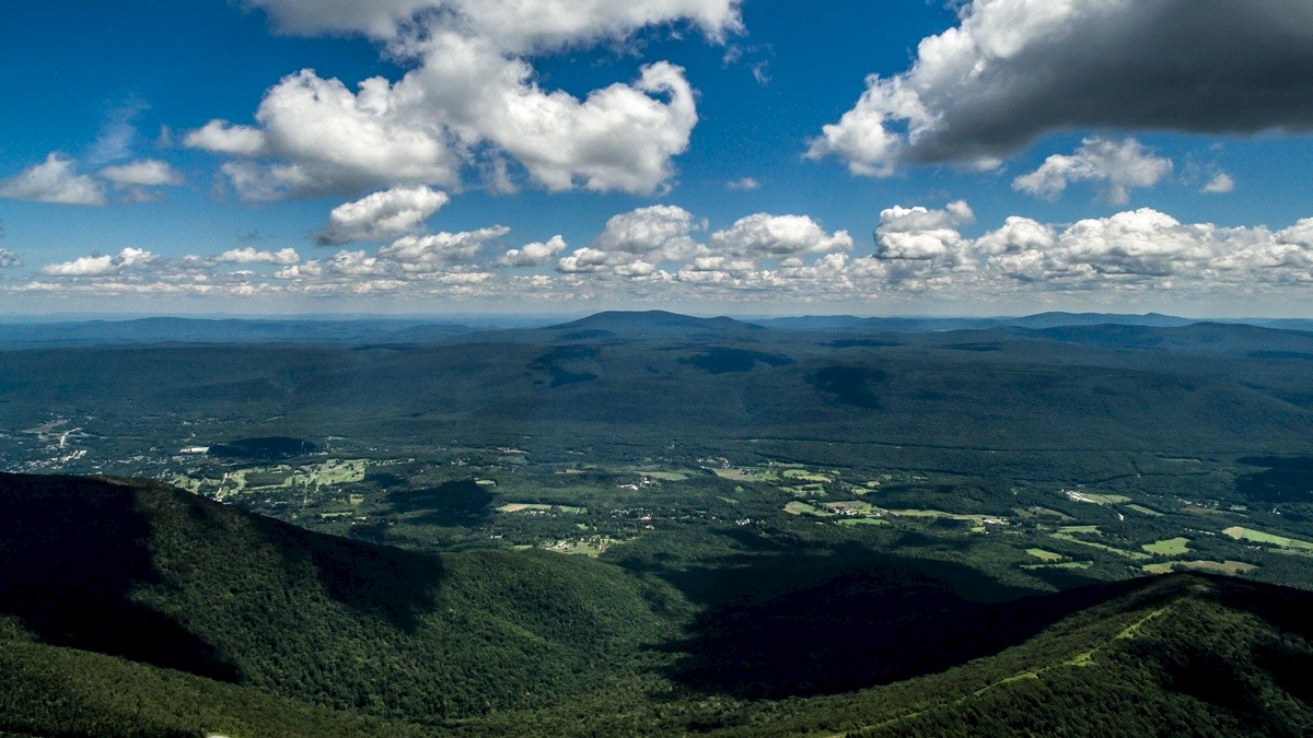 A scenic landscape with lush green hills, valleys, and scattered clouds in the sky, under bright daylight.