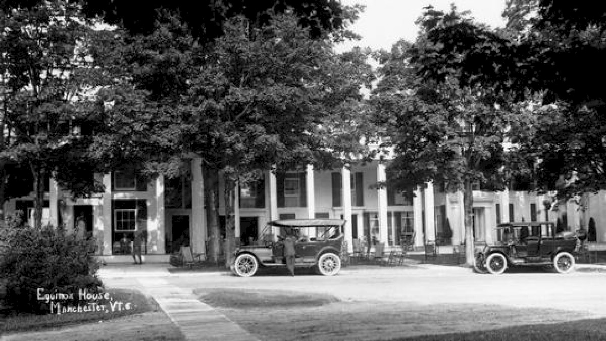 This black-and-white image shows a historic building with columns, identified as the Equinox House in Manchester, VT, with vintage cars parked in front.