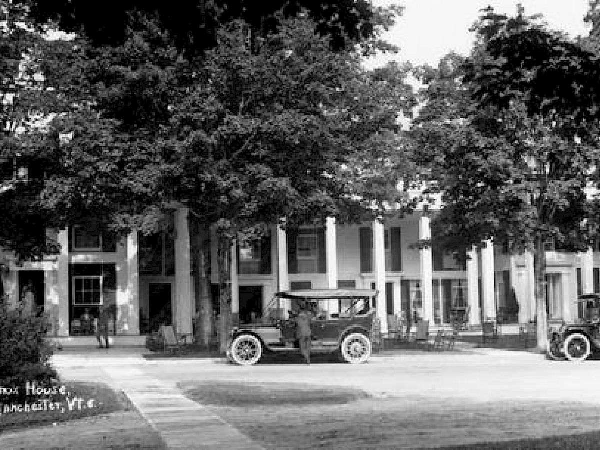 This black-and-white image shows a historic building with columns, identified as the Equinox House in Manchester, VT, with vintage cars parked in front.
