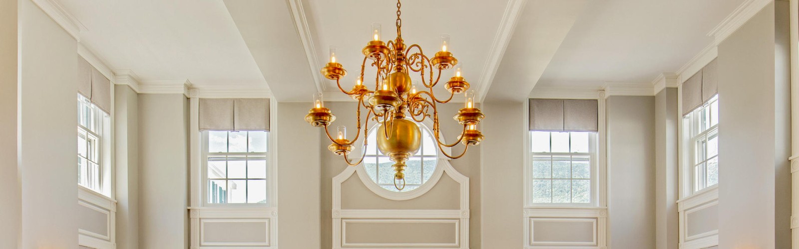 A spacious room with tall windows, light-colored walls, a large chandelier, and modern lamps near the windows, creating an elegant and airy space.