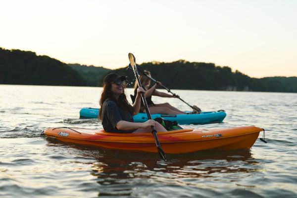 Two people are kayaking on a calm body of water at sunset, with one in an orange kayak and the other in a blue kayak.
